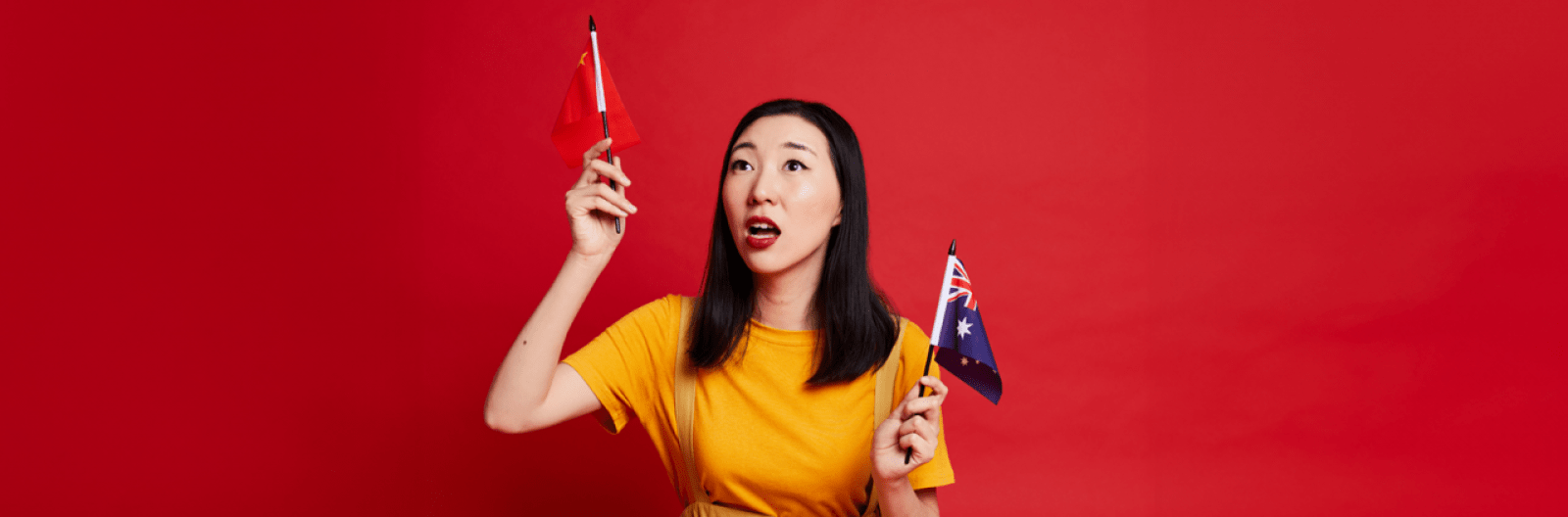 A woman dressed in a yellow top stands against a red background holding an Australian and a Chinese flag in each hand